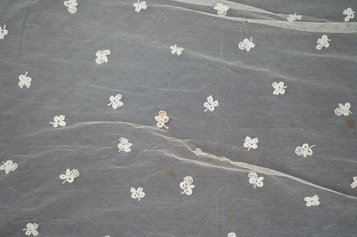 An Edwardian Brussels bobbin lace on net wedding veil, with all over bobbin lace appliqué spot motifs, within an ornate bobbin lace border, approximately 175cm x 168cm. Condition - there are various rust stains and holes